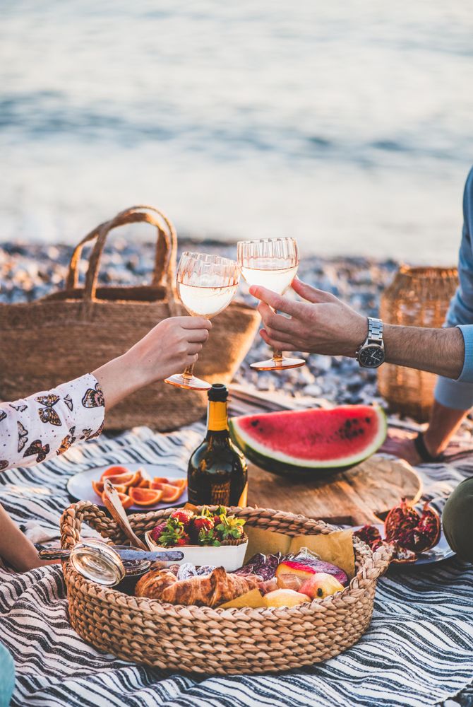 Two hands toasting with wine glasses over summer picnic by the ocean
