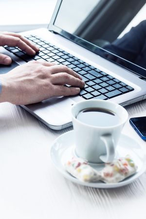 Person working on laptop on desk with cup of coffee