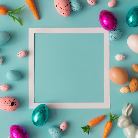 Easter composition made with colorful eggs on bright blue background with paper square outline