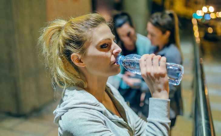 Portrait of tired woman drinking water after training with her friends at night