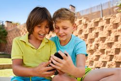 Cheerful boys browsing smartphone on sunbed