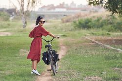 Cheerful young woman traversing park with bicycle