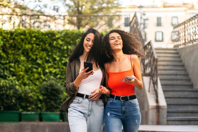 two stylish young woman walking and using smart phone