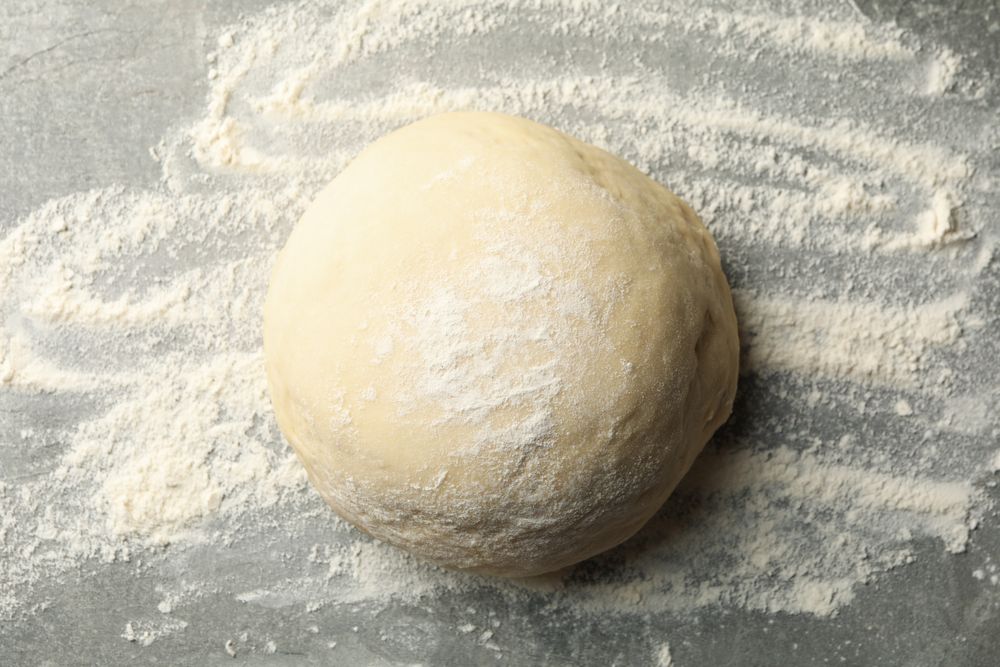 Dough ball and flour on gray background