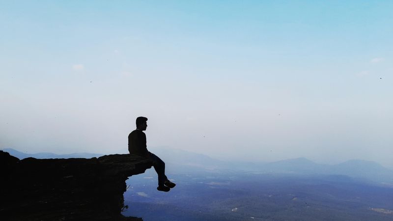 Silhouette of a man sitting on the edge of a cliff at nightfall