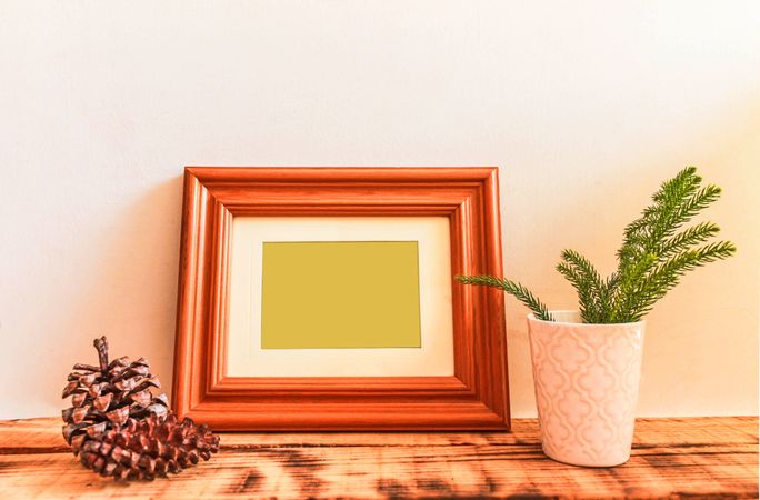 Wooden picture frame leaning against wall with branch and pinecone in vase mockup