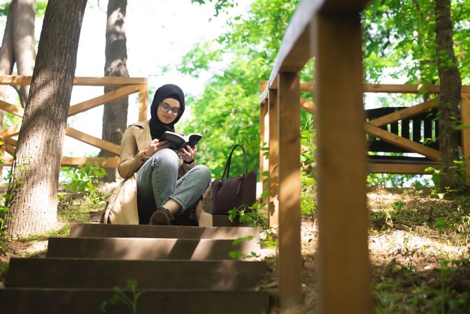 Middle Eastern woman in sunny park with a book on the steps