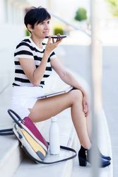 Female talking on speaker phone as laptop rests on her legs