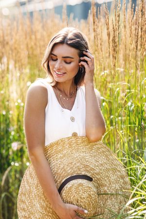 Woman adjusting hair in field of long grass with straw hat