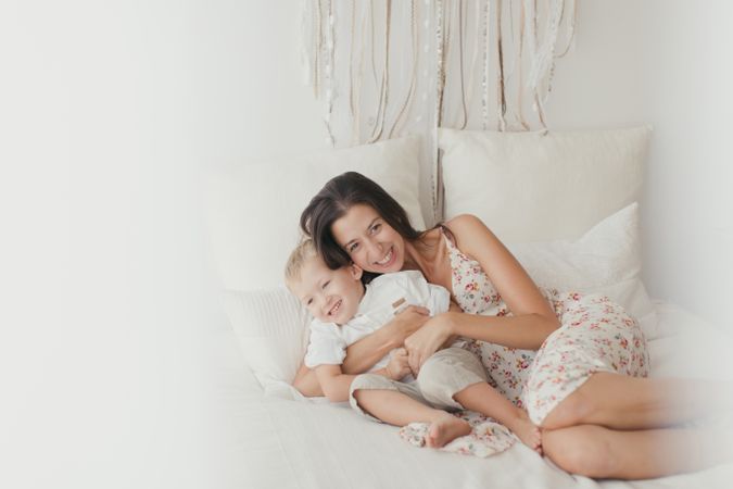 Mother ticking little son and laughing on bed