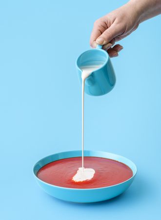 Pouring cream in tomato soup minimalist on a blue background