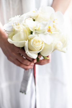 Hands of bride holding wedding bouquet with roses and orchids