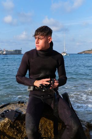 Serious young man in wetsuit with diving mask on stone