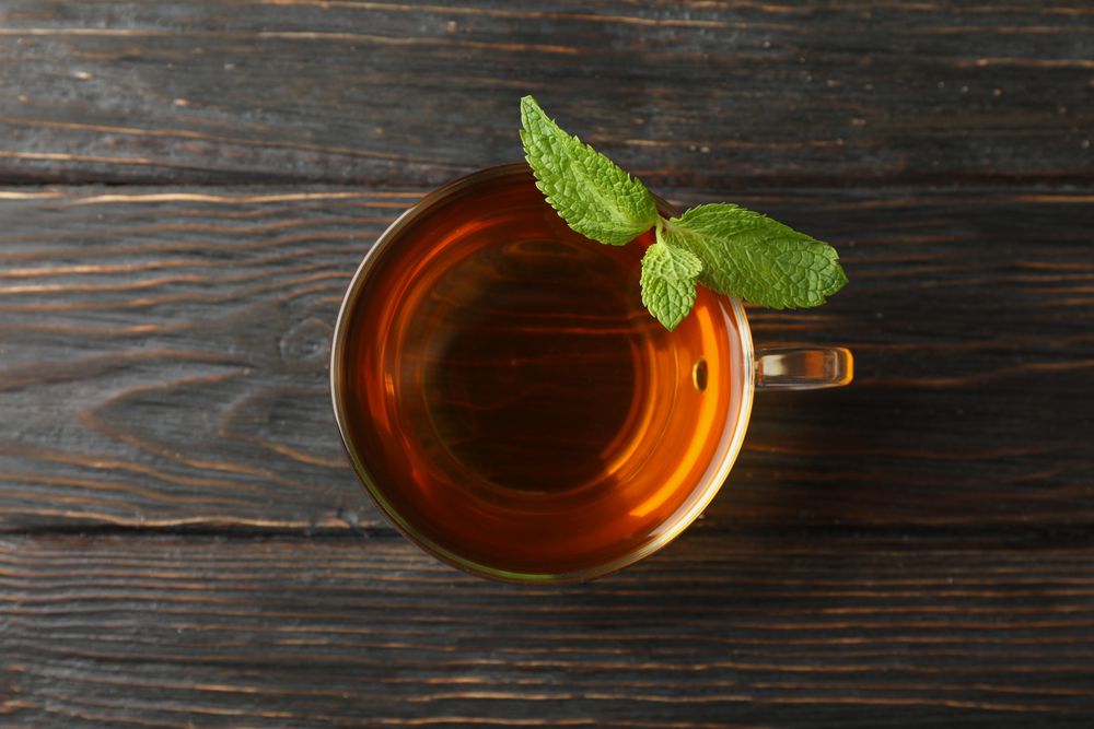 Cup of tea with mint on wooden background, top view