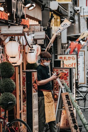 Young man with apron and facemask standing on sidewalk in Tokyo, Japan