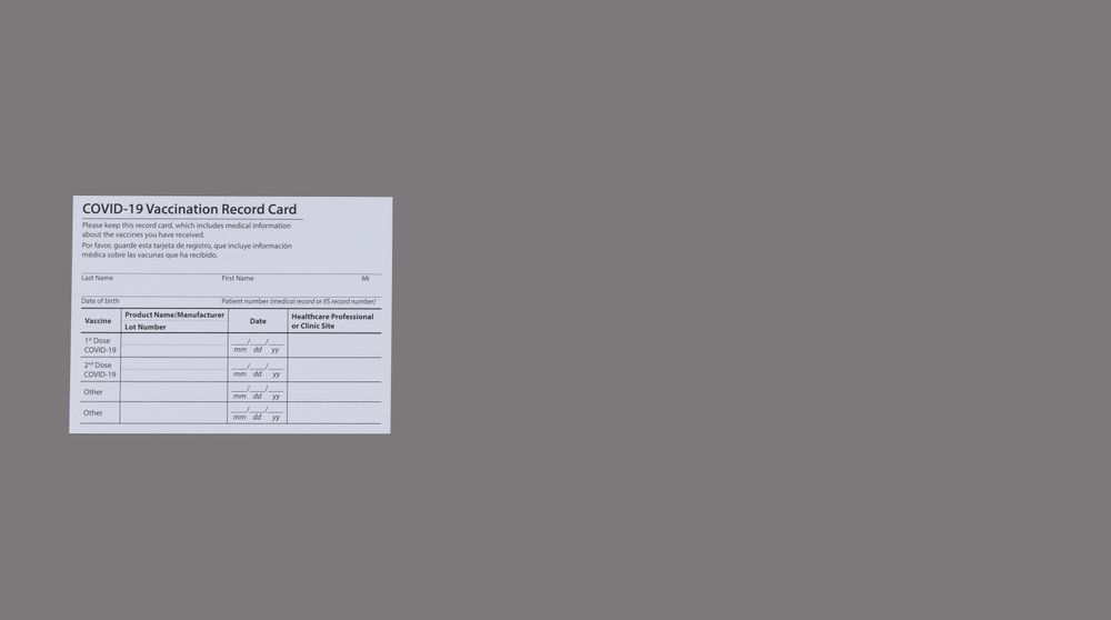 Covid 19 vaccination record card in both English and Spanish languages on a solid gray background with copy space