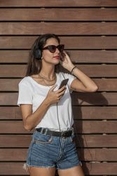 Woman using headphone to listen to music standing against wooden wall