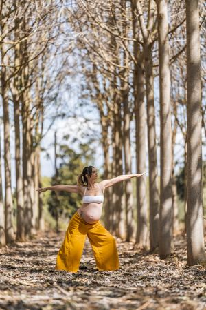 Concentrated adult expectant mother practicing yoga in park