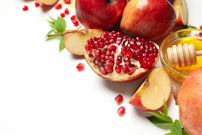 Close up of pomegranate with apples, honey and mint leaves lined up diagonally