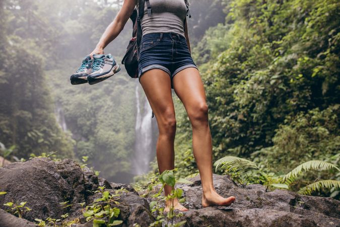 Female hiker walking barefoot on rock with waterfall in background