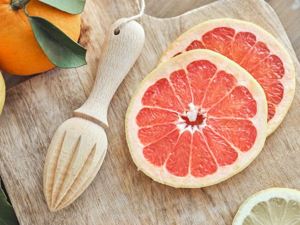 Sliced grapefruit and citrus reamer on wooden cutting board