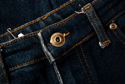 Close up gold and shiny button navy blue jeans fabric background texture.