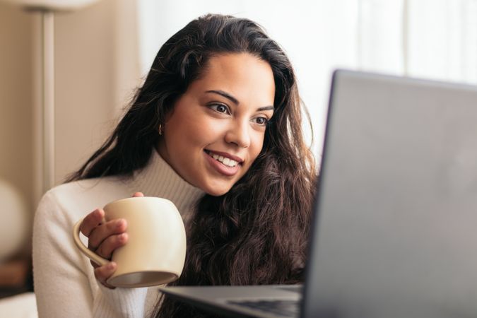 Young Woman Enjoying a Cup of Coffee While Using Laptop