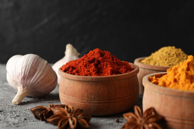 Side view of bowls of spices and garlic bulb, close up