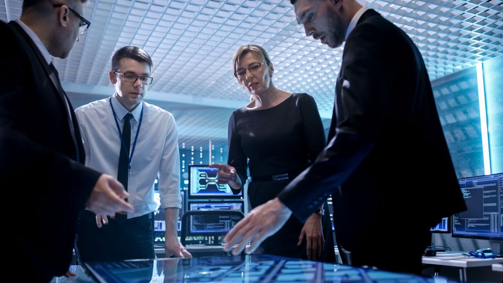 Team of Corporate Managers Working at the Table in Monitoring Room.