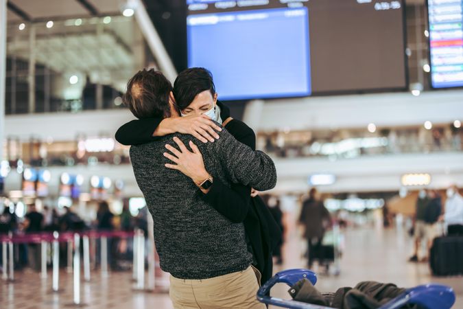 Man giving warm hug to his wife on arrival at airport in pandemic