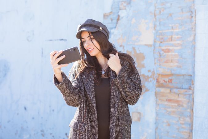 Charming Hispanic lady taking selfie near wall