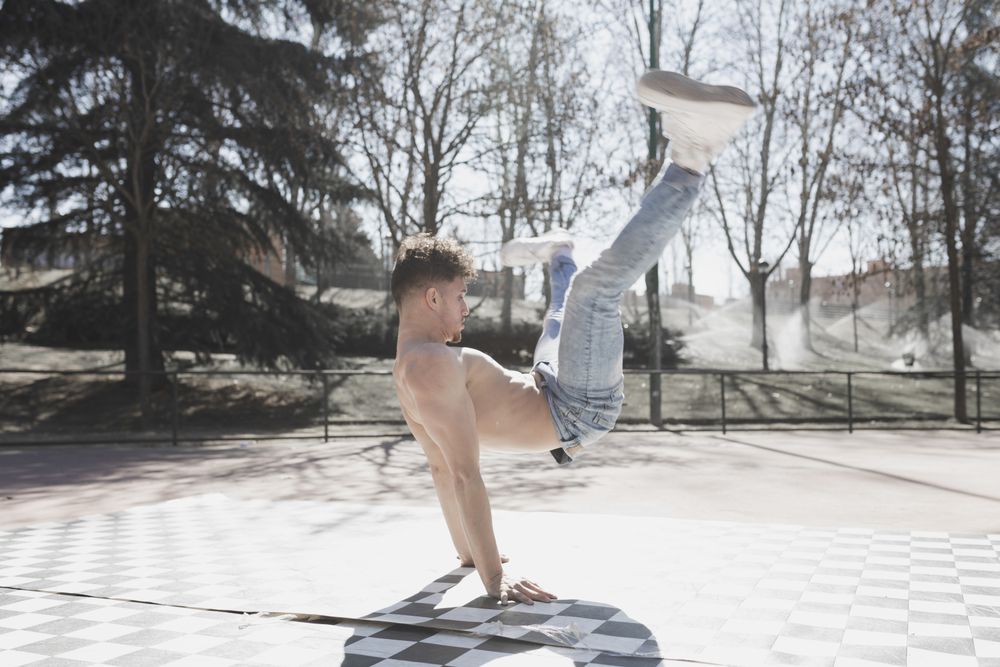 Shirtless man dancing break dance in park