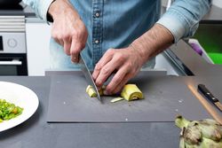 Man prepping artichoke on board with knife