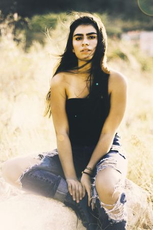 Portrait of woman in tank top and blue denim jeans sitting on ground outdoor