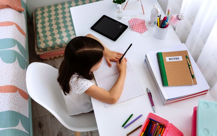 Girl studying at home with tablet and mask on table