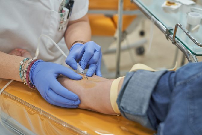 Crop female nurse making injection during blood donation in clin