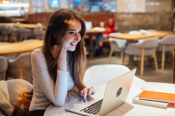 Brunette woman in a restaurant smiling while looking up from her laptop