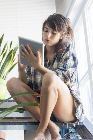 Female in flannel shirt lounging in bright home with digital tablet