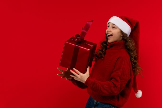 Excited girl in Santa hat catches large red Christmas gift.