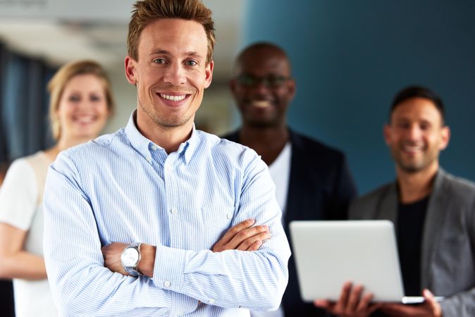 Smiling man with arms crossed pictures in front of colleagues