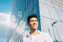 Smiling young man in sunlight under skyscraper