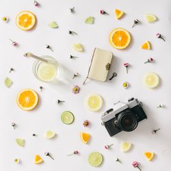Colorful pattern made of orange, lemon, lime and flowers with lemonade and camera and notebook