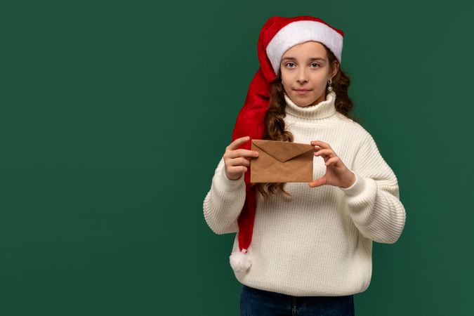 Girl in Santa hat holding brown envelope with serious expression.