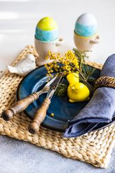 Easter table setting with navy plate with bird ornament and decorative eggs in cups