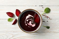 Looking down at bowl of borscht or beetroot soup on wooden table with slices on the side