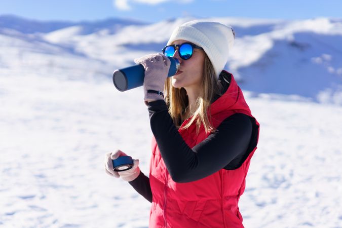 Woman in red snowsuit sipping from water bottle on snowy mountain
