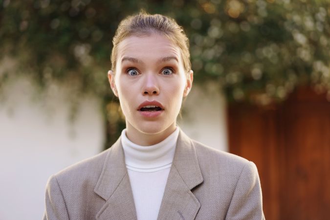 A surprised woman wearing a stylish outfit against a beautiful outdoor background scene
