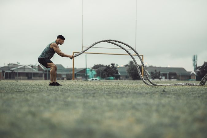 Athlete working out with battle ropes outdoors on grass field