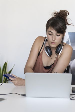 Female typing on laptop with headphones around her neck