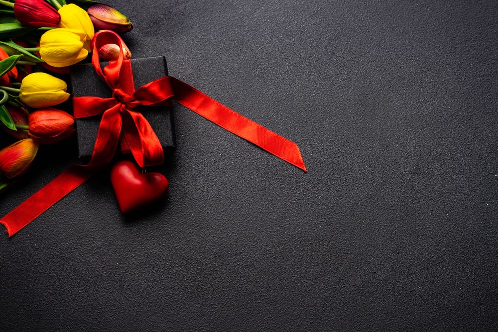 Fresh tulips and present with red ribbon on dark table with copy space